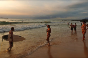 Nudists and Surfers frolic on a nude beach.